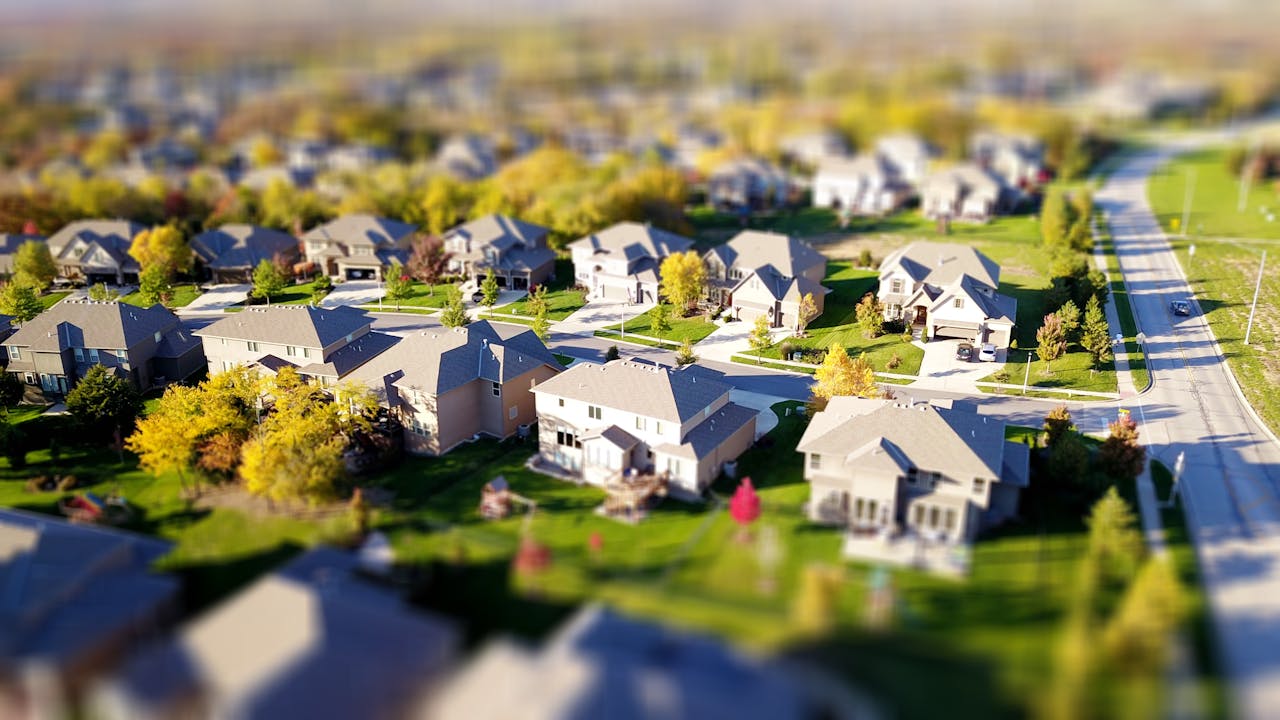digital Tilt-shift aerial photo of a suburban neighborhood with green lawns and roads.
